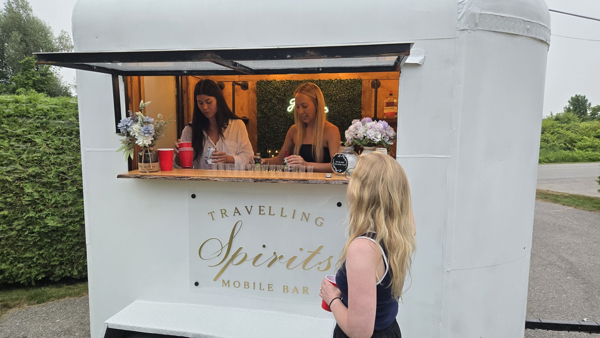 Bartenders pouring cocktails from Travelling Spirits mobile bar trailer during a daytime outdoor wedding